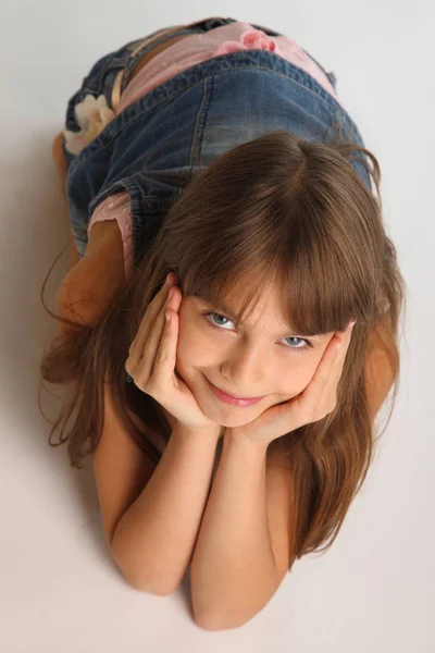 一个穿着牛仔短裤的漂亮女孩的肖像躺在地板上 可爱的笑脸 漂亮的孩子 这个年轻的女学生9岁了 — 图库照片