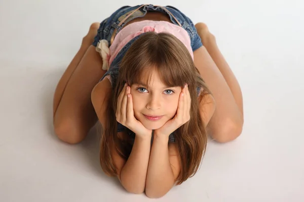 Güzel kız kot şort yere yalınayak dinleniyor. İnce bir gövde ve çıplak uzun bacaklar ile zarif çekici çocuk. Genç kız öğrenci 9 yaşında.