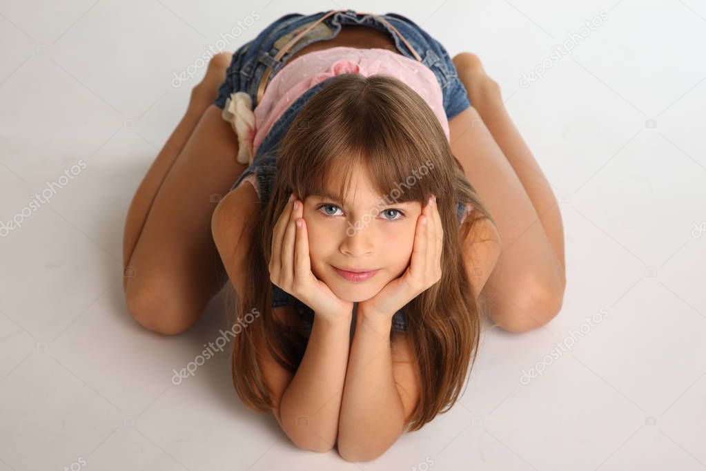 Beautiful girl in a denim shorts is resting on the floor barefoot. Elegant attractive child with a slender body and bare long legs. The young schoolgirl is 9 years old.