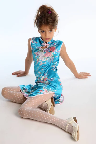 穿着亚洲蓝色连衣裙的漂亮女孩正坐在白色的背景上 优雅迷人的孩子与细长的身体和长腿在白色丝袜 9岁时装风格的年轻模特 — 图库照片