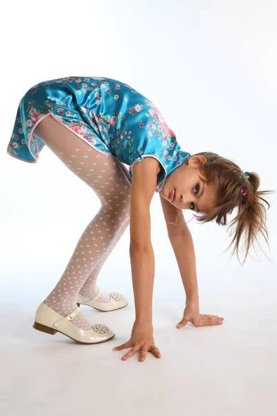 Bir Asya mavi elbiseli güzel kız beyaz bir arka plan üzerinde duruyor. İnce bir vücudu ve uzun bacaklar beyaz külotlu çorap zarif çekici çocuk. Genç moda stil 9 yaşında model.