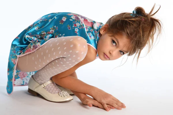 Beautiful girl in an asian blue dress is sitting on a white background. Elegant attractive child with a slender body and long legs in white pantyhose. The young model 9 years old in fashion style. — Stock Image Beautiful Girl Asian Blue Dress Sitting White Background Elegant Attractive Royalty Free Stock Images