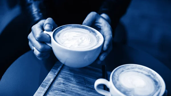 Person\'s hands holding a cup of hot cappuccino at cafe while dri
