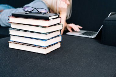 Blond hair Woman lying on black sofa using laptop in living room