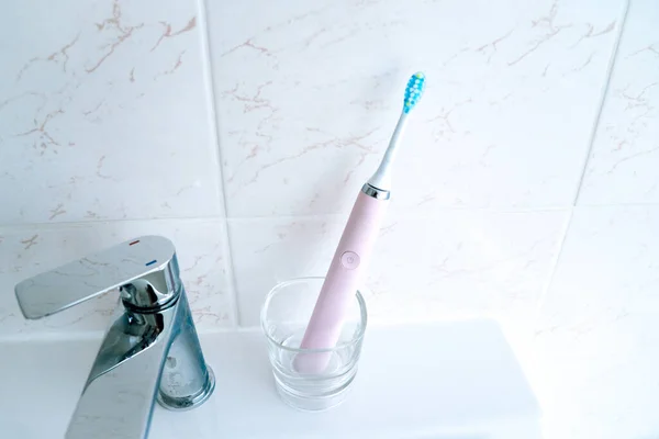 Розовые электрические зубные щетки и стекло в ванной комнате дома . — стоковое фото
