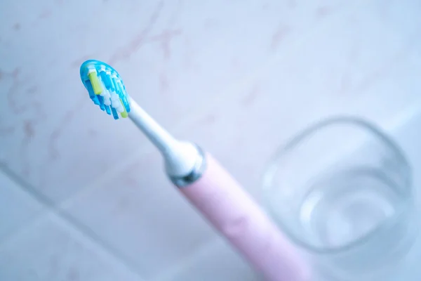 Pink electric toothbrushes and glass in the bathroom at home. — Stock Photo, Image