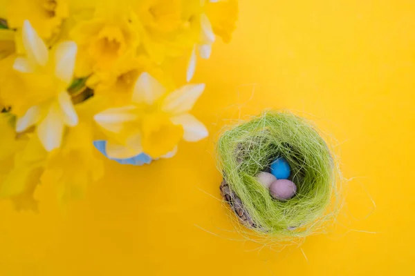 Easter holiday decorations on yellow background. Colorful easter painted speckled eggs in basket. Creative spring composition with Easter elements - flowers and eggs. Traditional Easter Celebrating.