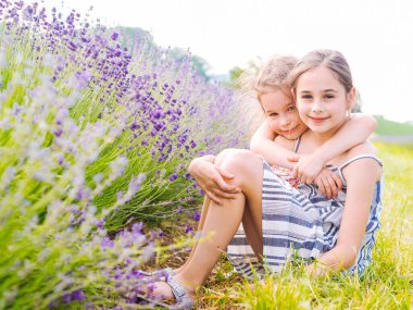 İki kız kardeş Provence 'deki lavanta tarlalarının arasında oturuyor. Yaz güneşinde açan mor lavanta tarlaları. Leylak Çiçekleri Denizi manzarası. Fransız Kaynağı 'nın kokulu çiçekleri.