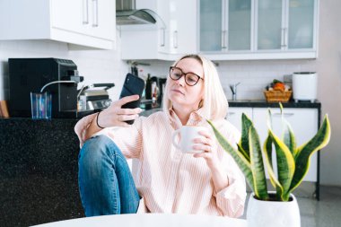 Mutfakta oturan mutlu bir kız ve elinde video çağrısı var. Genç bir kadın, arkadaşıyla ya da ailesiyle görüntülü konuşma yapmak için akıllı telefonu kullanıyor. Vlogger webinar kaydediyor. Kadın kameraya bakıyor ve el sallıyor.. 