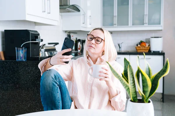 Mutfakta oturan mutlu bir kız ve elinde video çağrısı var. Genç bir kadın, arkadaşıyla ya da ailesiyle görüntülü konuşma yapmak için akıllı telefonu kullanıyor. Vlogger webinar kaydediyor. Kadın kameraya bakıyor ve el sallıyor.. 