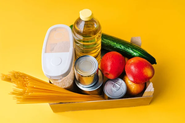 Food supplies. Crisis food box stock for coronavirus quarantine isolation period in wood background. Different food in aluminum cans, Rice, pasta, oil, fruit, vegetable. Food delivery, Donation.