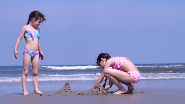 一緒にビーチビル砂の城で遊ぶ夏休みの子供たち 海岸で砂の城を作る子供たち カラフルな帽子と水着を身に着けている美しい女の子は海岸で遊ぶのを楽しむ — ストック動画