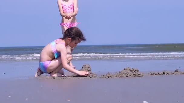 一緒にビーチビル砂の城で遊ぶ夏休みの子供たち 海岸で砂の城を作る子供たち カラフルな帽子と水着を身に着けている美しい女の子は海岸で遊ぶのを楽しむ — ストック動画