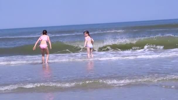 カラフルな帽子と水着を身に着けている美しい女の子は熱帯のビーチで遊ぶのを楽しむ 海岸で暖かい水しぶきを楽しむ子供たち 子供たちは海岸で暖かい晴れた日に波に飛び乗る — ストック動画
