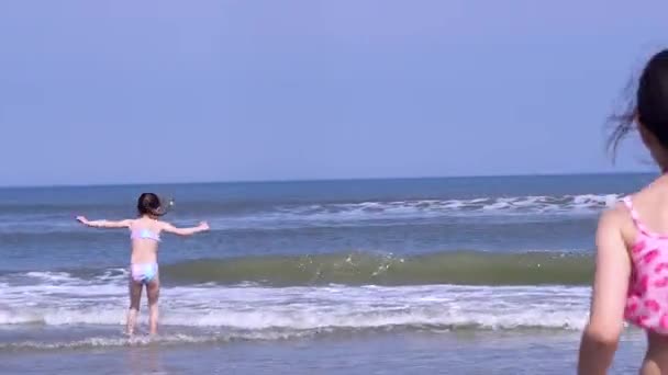 カラフルな帽子と水着を身に着けている美しい女の子は熱帯のビーチで遊ぶのを楽しむ 海岸で暖かい水しぶきを楽しむ子供たち 子供たちは海岸で暖かい晴れた日に波に飛び乗る — ストック動画