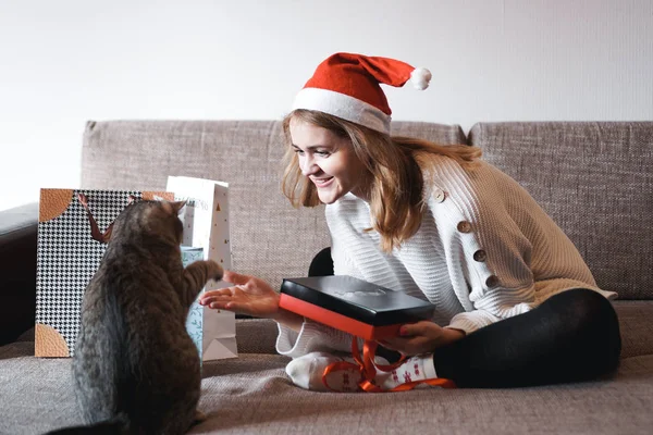 Chica feliz en santa hat apertura de la caja de regalo de Navidad y jugando con el gato —  Fotos de Stock