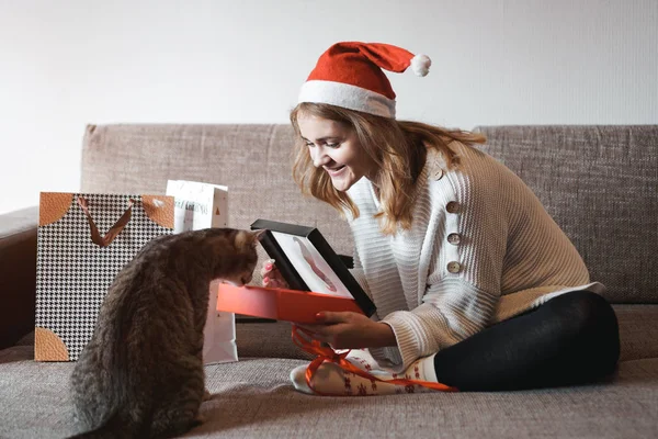 Chica feliz en santa hat apertura de la caja de regalo de Navidad y jugando con el gato —  Fotos de Stock
