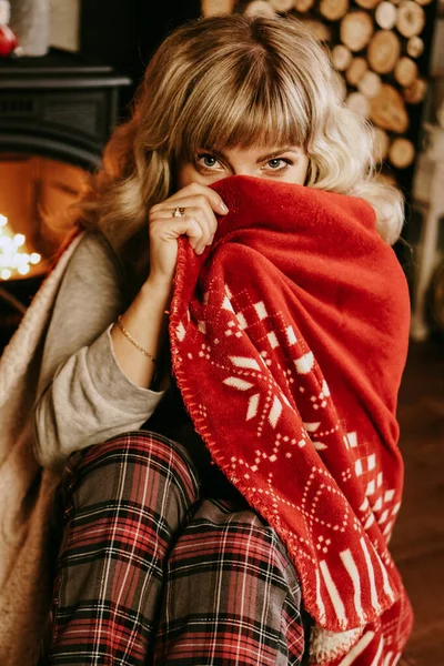 Una hermosa joven en una tela escocesa roja se sienta en el cálido interior clásico de Año Nuevo —  Fotos de Stock