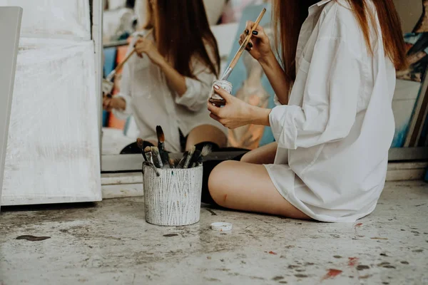 Una pintora sentada en el suelo frente al espejo. Interior del estudio de arte —  Fotos de Stock