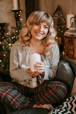 Noel 'i kutlayan bir mum tutarken gülümseyen çekici bir genç kadın.