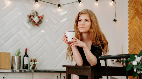 Mulher segura uma xícara de café pela manhã na cozinha de Natal — Fotografia de Stock