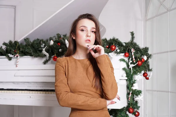 Hermosa chica con el pelo largo cerca de un piano blanco con decoración de Navidad — Foto de Stock