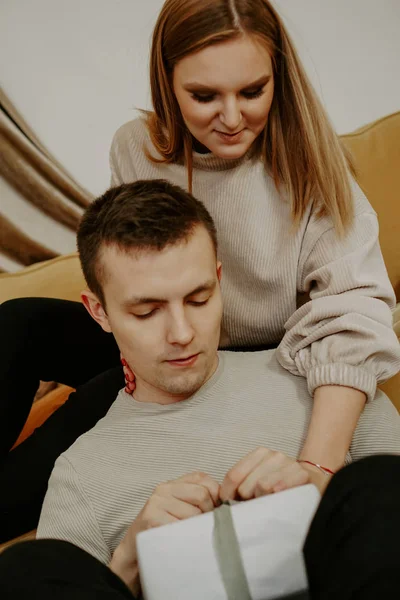 Красива молода пара тримає подарункову коробку, сидячи на дивані вдома — стокове фото