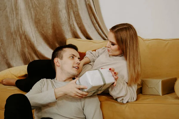 Schönes junges Paar hält eine Geschenkbox, während es zu Hause auf der Couch sitzt — Stockfoto