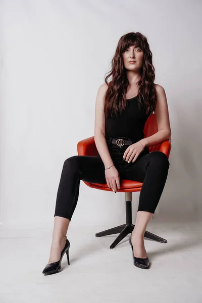 Menina bonita nova no terno de negócios sentado na cadeira vermelha, fundo branco — Fotografia de Stock