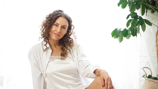 Retrato de una hermosa mujer sentada en casa con plantas y sonriendo a la cámara — Foto de Stock