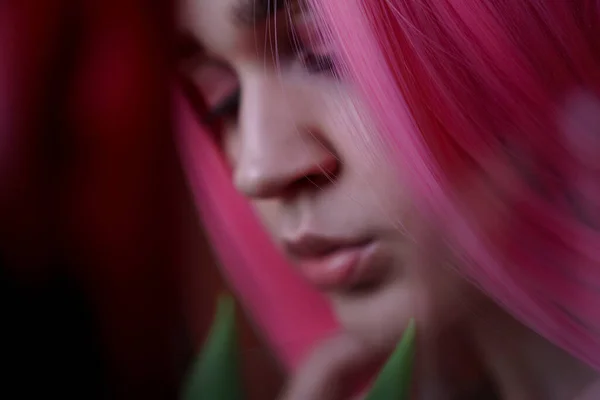 Девушка с розовыми волосами и цветами близко к лицу. Не в фокусе, размытый фон — стоковое фото
