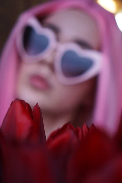 Chica con el pelo rosa con flores cerca de la cara. Fuera de foco, fondo borroso —  Fotos de Stock