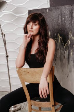 Güzel esmer bir kadının portresi gri bir arka planda bir sandalyede oturuyor.