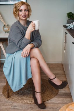 Gülümseyen sarışın kapuçino içiyor, elinde kahve fincanı tutuyor.