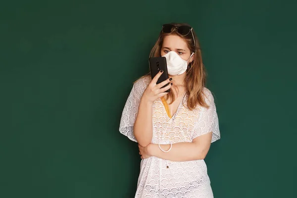 Chica turista en una máscara médica con el teléfono en las manos sobre un fondo verde —  Fotos de Stock