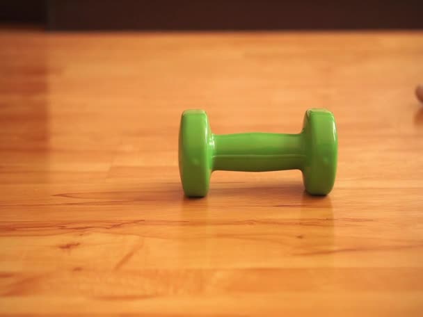 Girl takes a break in training and puts a dumbbell on a wooden floor — Stock Video