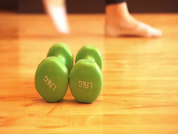女孩从木地板上拿了两个哑铃进去健身 — 图库视频影像