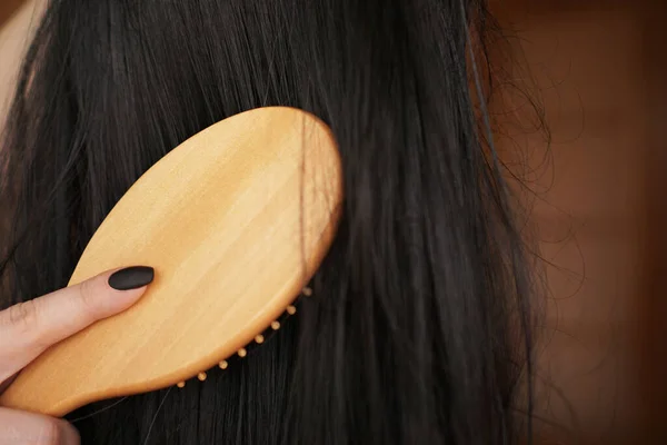 Die weibliche Hand hält eine schwarze Perücke mit langen Haaren und kämmt einen Holzkamm — Stockfoto