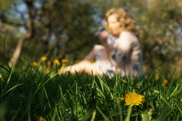 Cute kobieta odpoczynek w parku z mniszkami lekarskimi - skupić się na kwiat w trawie — Zdjęcie stockowe