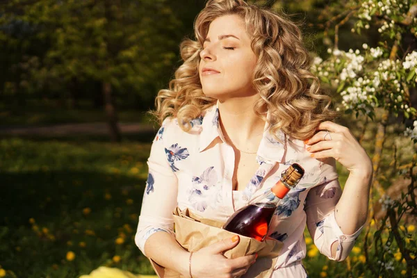 Mulher bonita segurando uma garrafa de vinho em branco enquanto almoça ao ar livre — Fotografia de Stock
