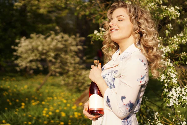 Красивая молодая женщина держит пустую бутылку вина во время обеда на открытом воздухе — стоковое фото