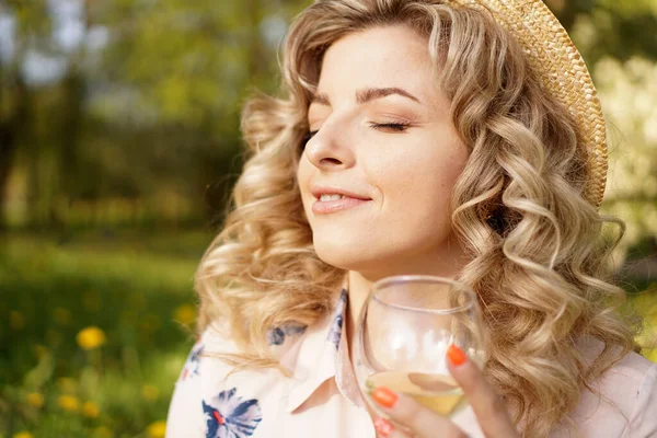 Счастливая блондинка с бокалом белого вина во время пикника на закате в парке — стоковое фото