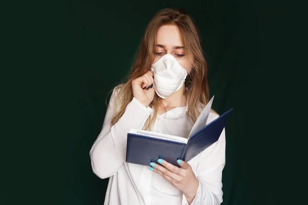 Chica joven con una máscara médica en una blusa de oficina blanca con un cuaderno en la mano — Foto de Stock