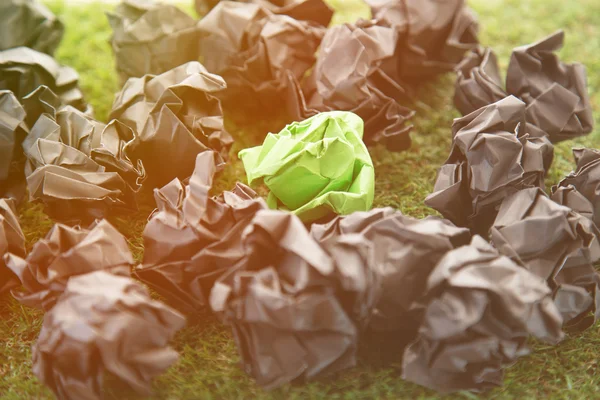 Papel esmigalhado verde entre bolas de papel preto na grama field.jp — Fotografia de Stock