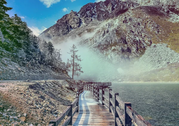 WOODEN BRIDGE near smooth water of Mugecuo Lakes China landscape — стоковое фото