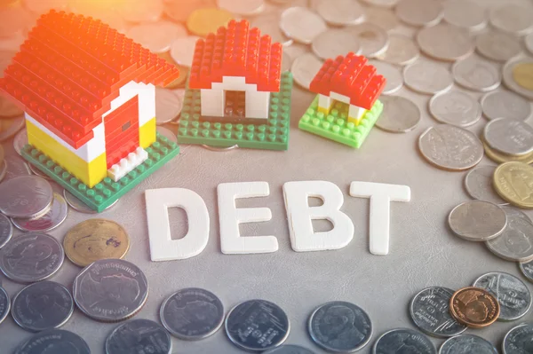 Schulden hölzernen Text und Reihen von Münzen mit Hausmodell — Stockfoto