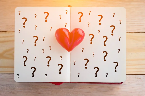 Book with opened pages and clay heart with question mark symbol