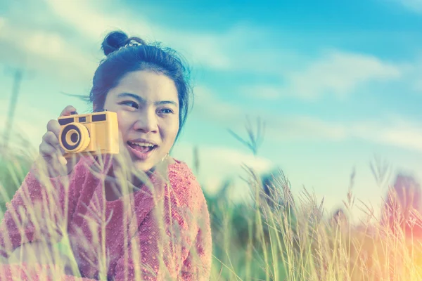 asian girl holding a retro camera in grass field with clear open blue sky vintage color tone