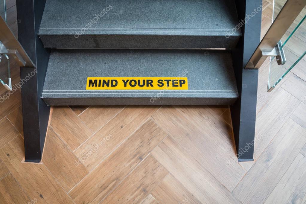 Yellow And Black Warning Sign On Stairs Stating "Watch Your Step.