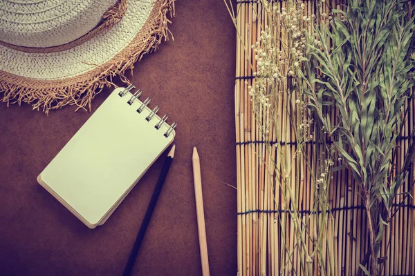 棕色皮革背景光眩光效果与旅行概念与干燥花与藤自然帽子和树与空白页笔记本和铅笔 — 图库照片